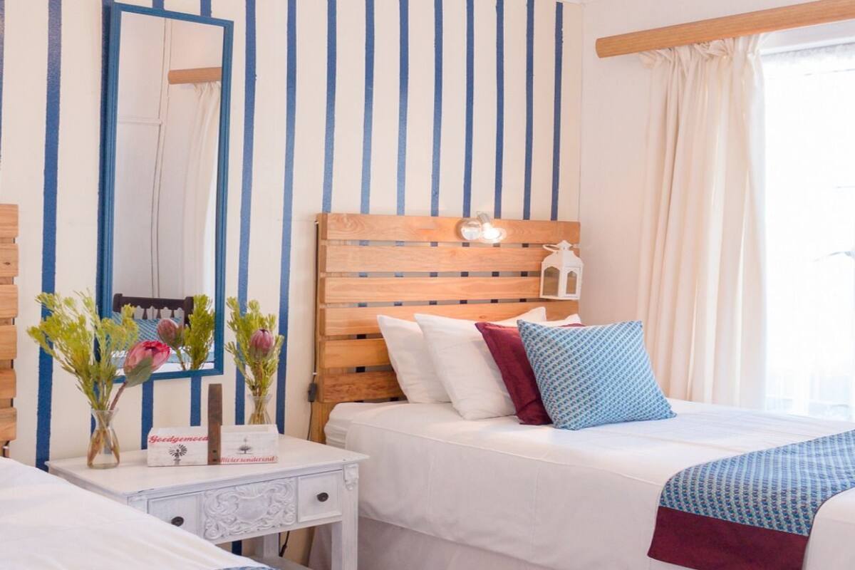 A hotel room with a wooden headboard, a bedside table with a lamp, and a bed with white bedding and colorful pillows.