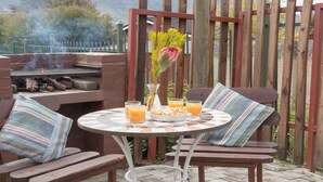 An outdoor patio with a round table, two chairs, a grill, and a view of mountains. - Mooigezicht (Clarens)