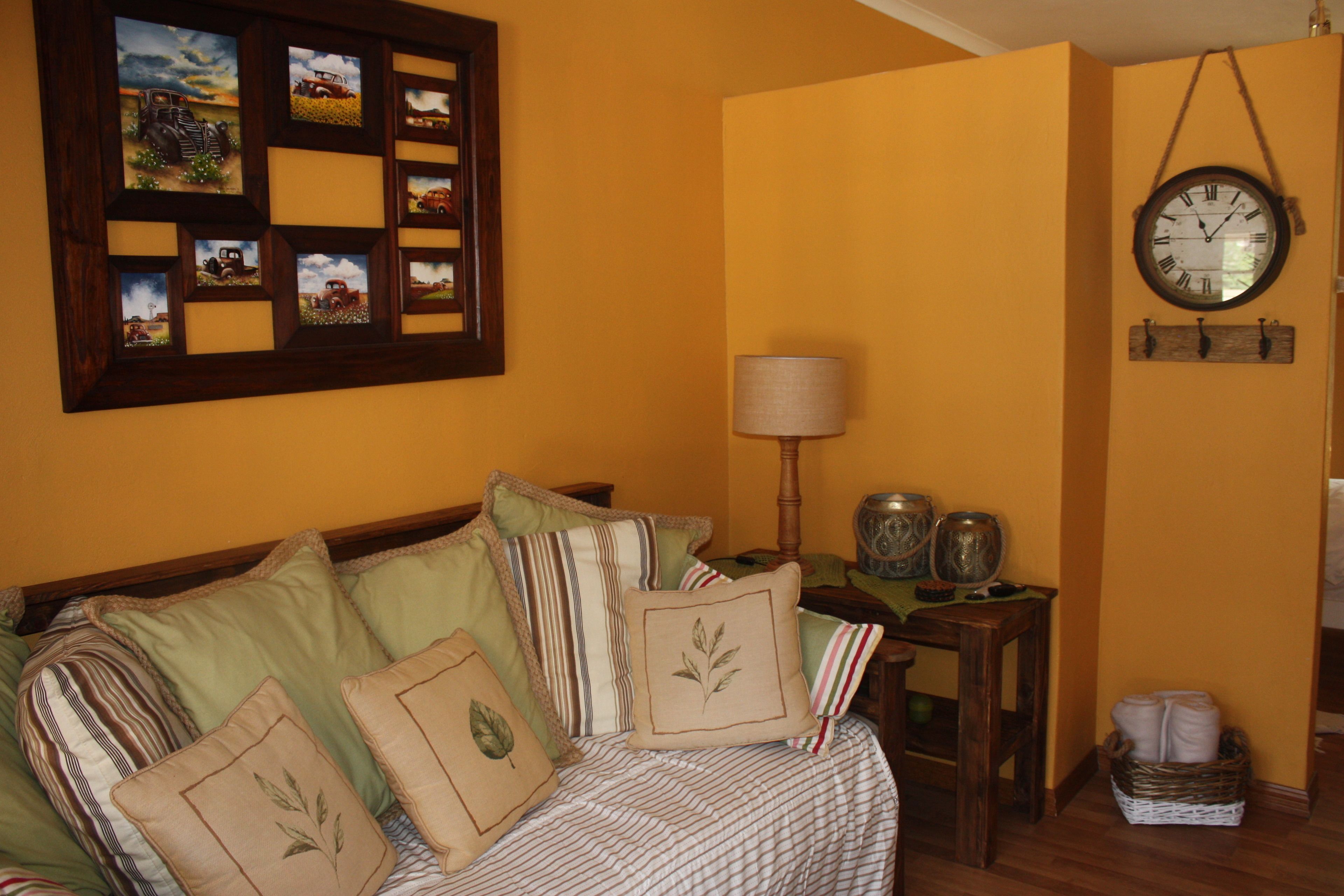 A bedroom with a bed, pillows, a wall clock, a lamp, and a small table with decorative items.