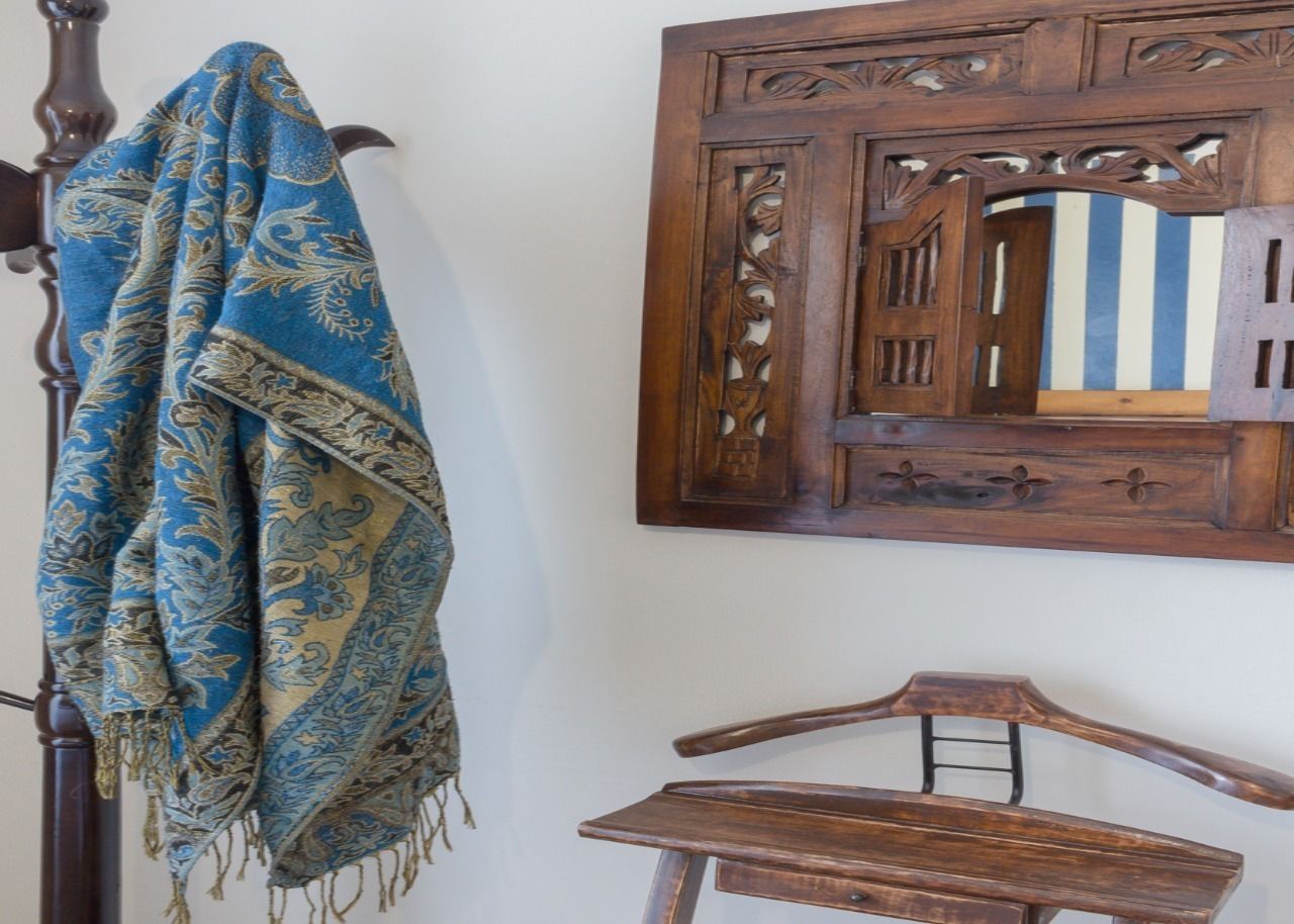A wooden bed with a headboard, a wooden chair, and a wall-mounted mirror with intricate carvings.
