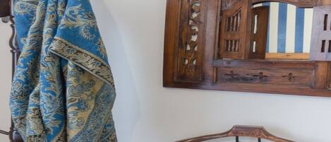 A wooden bed with a headboard, a wooden chair, and a wall-mounted mirror with intricate carvings.
