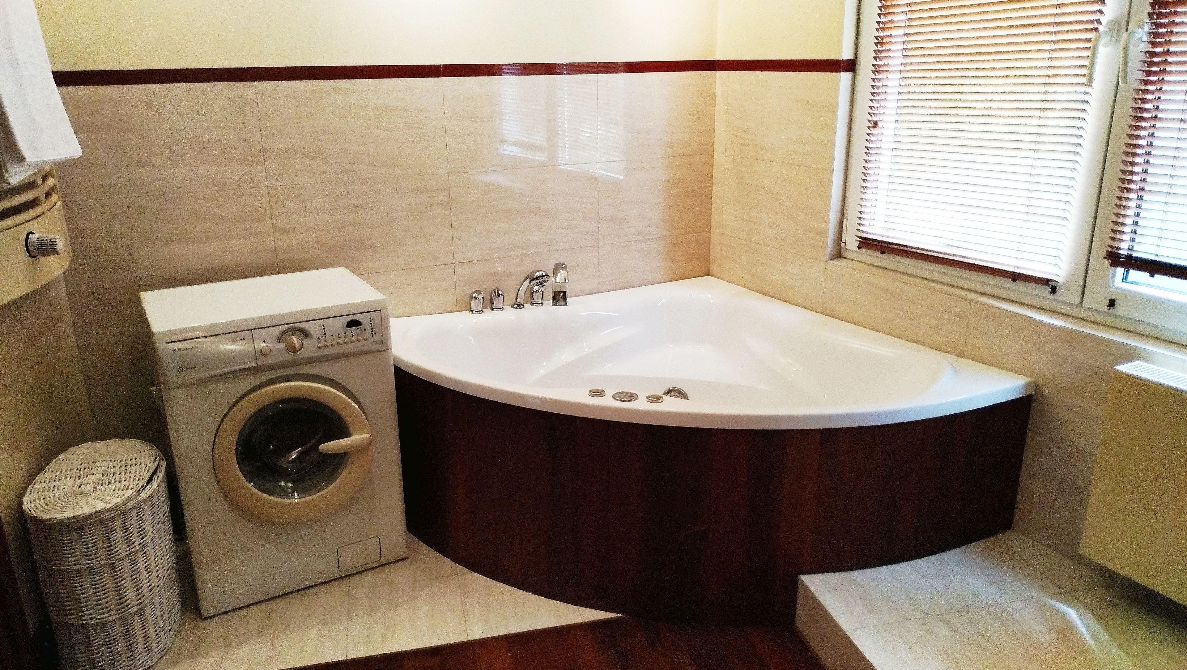 Un baño con lavadora, bañera y ventana con persianas.