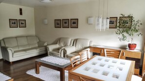 A living room with a beige sofa, a wooden dining table, and a potted plant. - Apartament Królewski Sandomierz (Sandomierz)