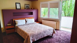 A bedroom with a bed, a nightstand, a dresser, a window with a view of greenery, and two framed pictures on the wall. - Apartament Królewski Sandomierz (Sandomierz)