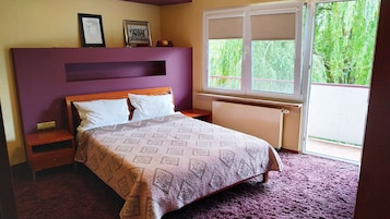 Quarto com cama, mesa de cabeceira, penteadeira, janela com vista para o verde e duas quadros na parede.