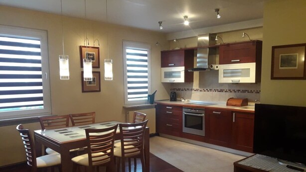 A compact kitchen with a dining area, featuring a built-in oven, microwave, and a TV on a wooden stand. - Apartament Królewski Sandomierz (Sandomierz)