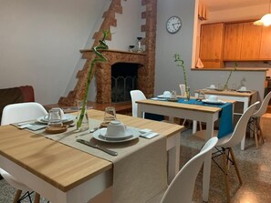Un coin repas avec des tables et des chaises en bois, une cheminée et une horloge au mur.