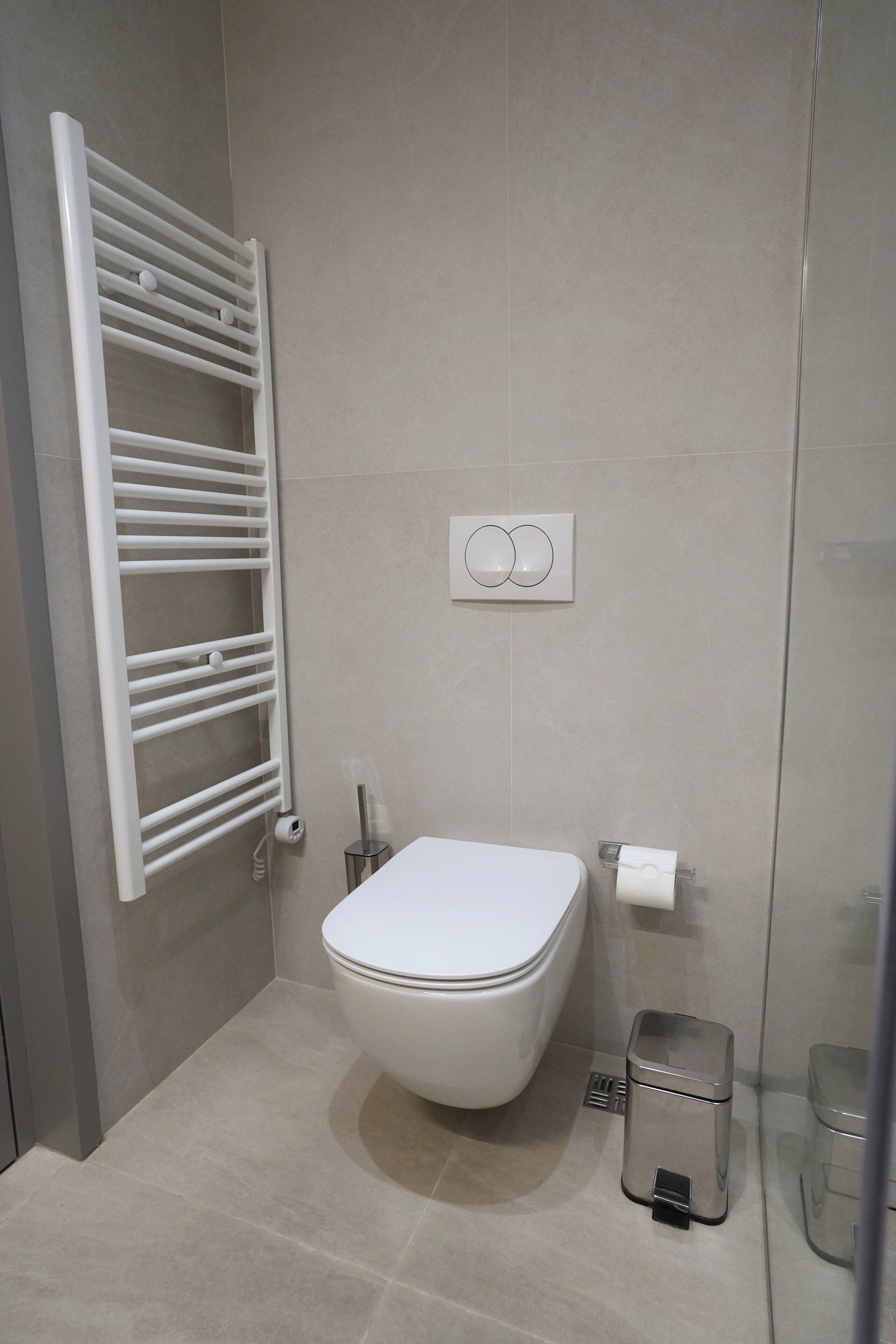Et moderne badeværelse med toilet, håndklædeholder på væggen og en lille skraldespand.