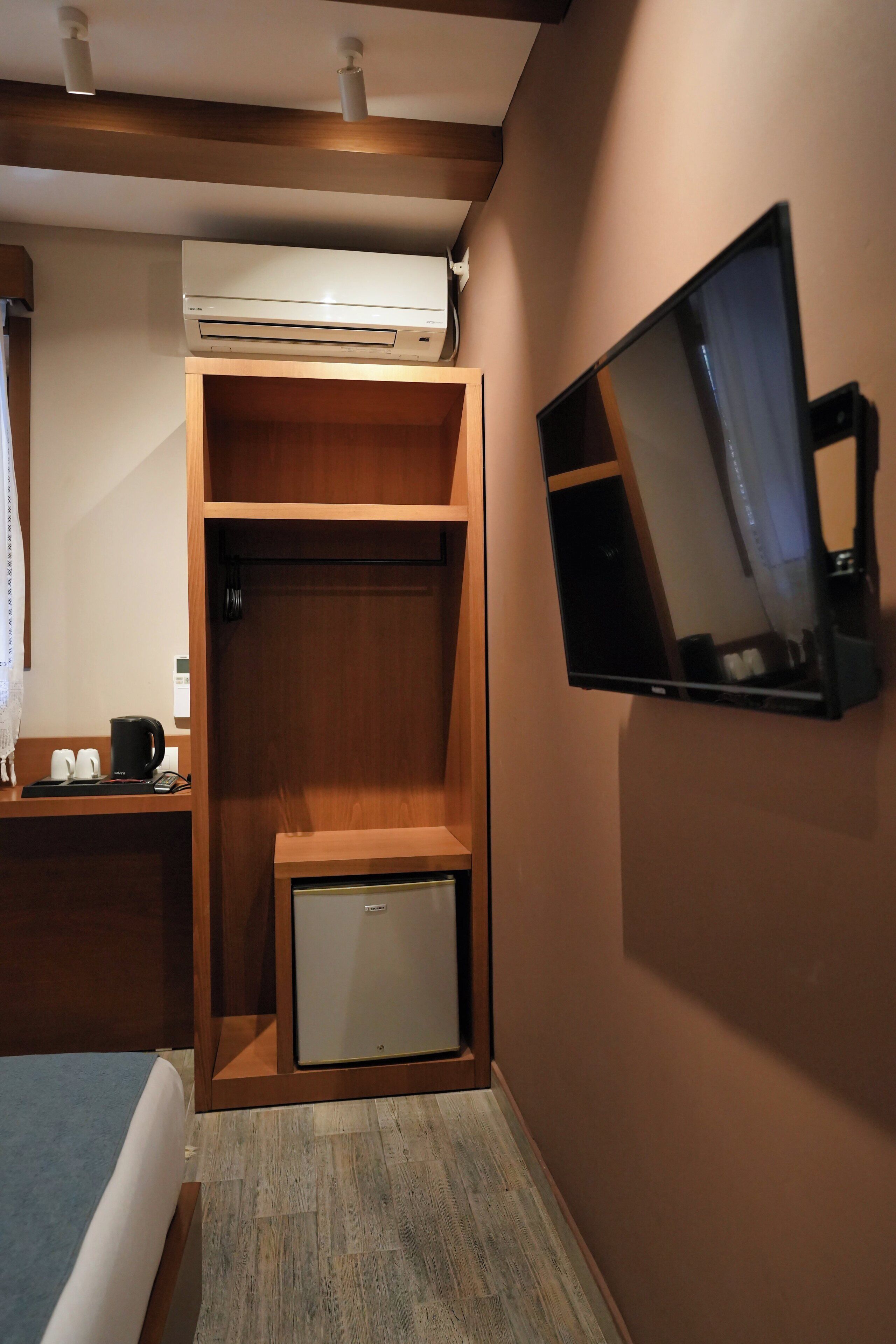Habitación de hotel con una cama, un escritorio con cafetera, un televisor montado en la pared y un mueble pequeño.