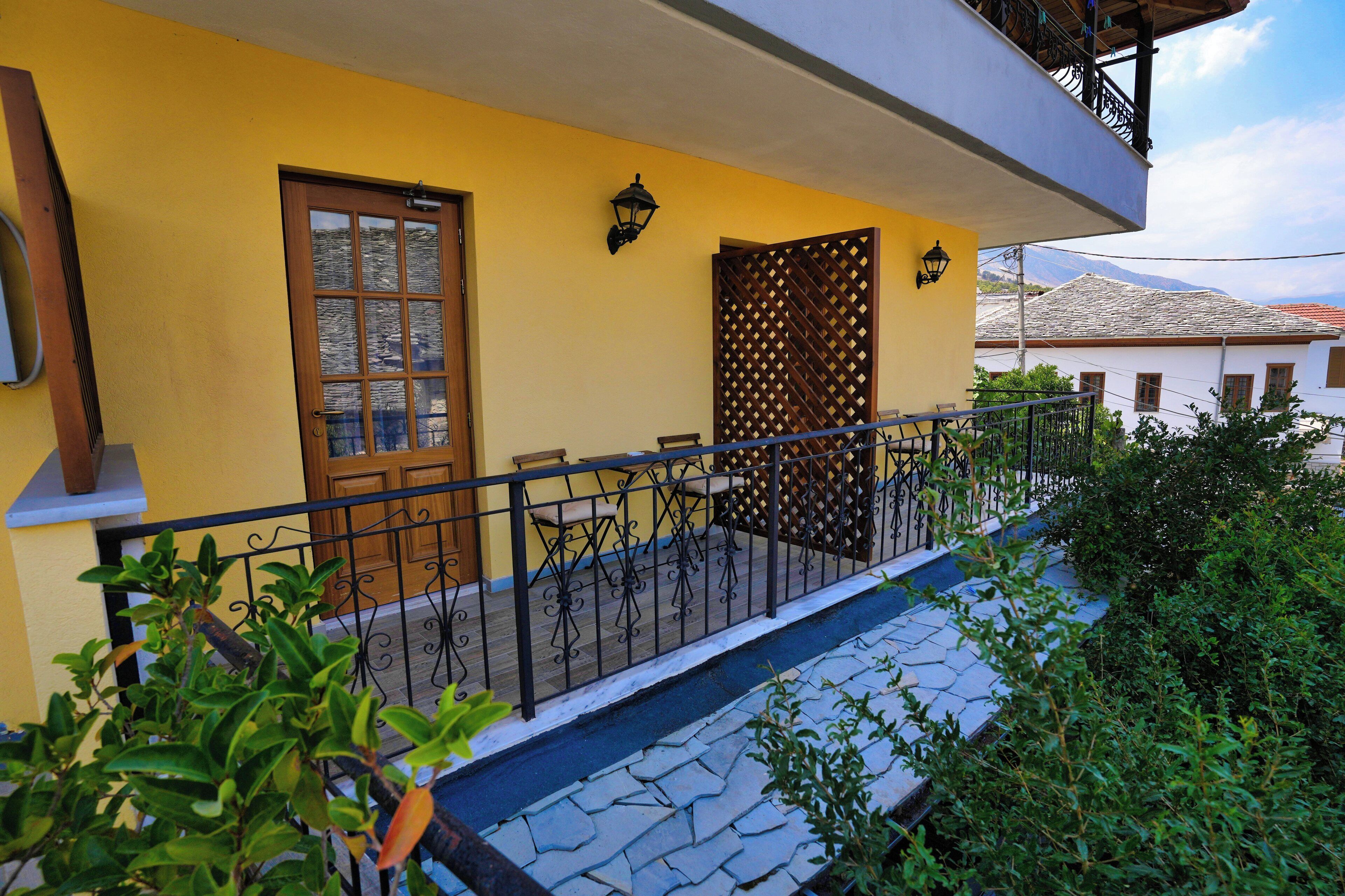 Un bâtiment jaune avec une porte en bois, un balcon doté d’une rambarde en métal et un chemin pavé de pierres.