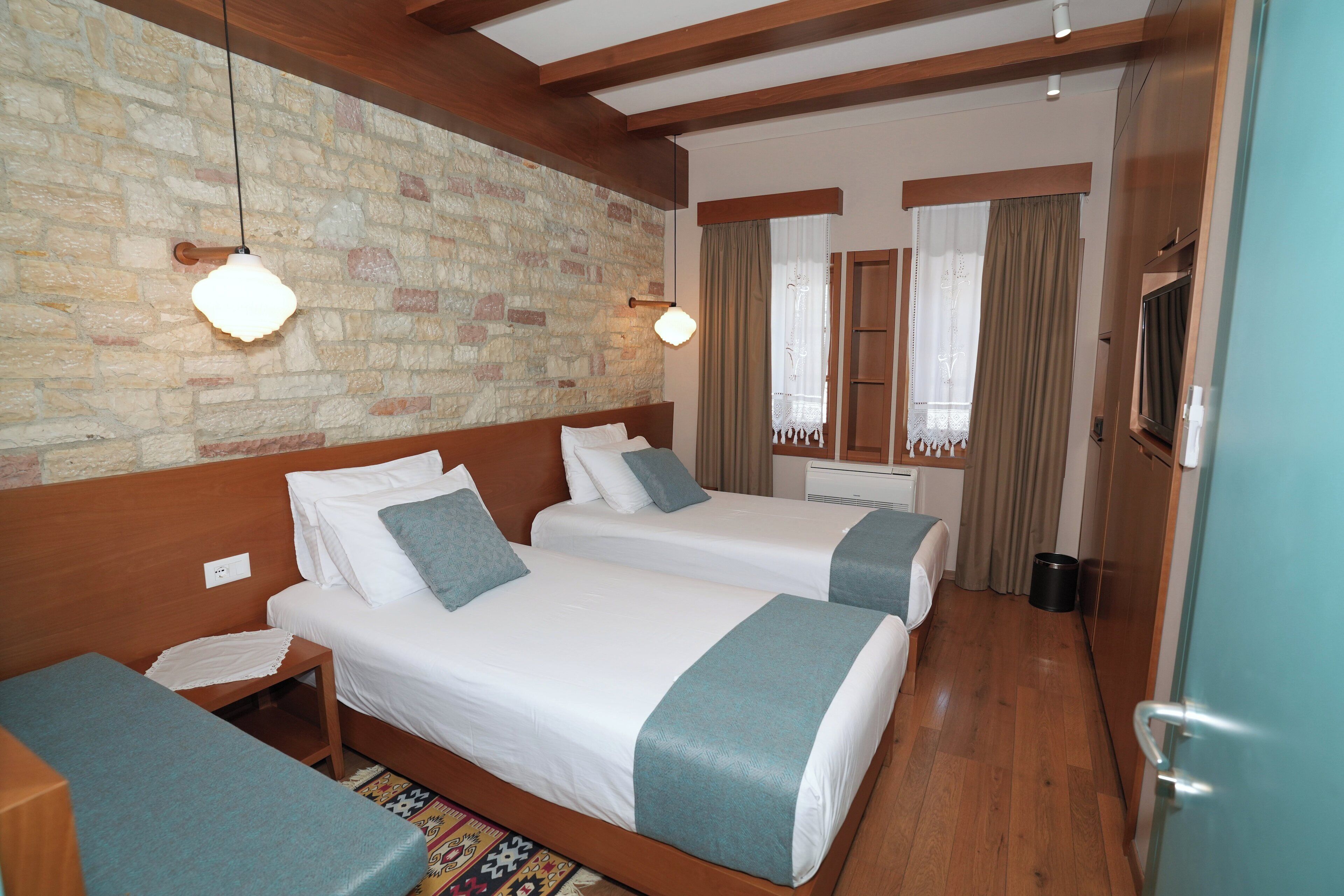 Habitación de hotel con dos camas, techo de madera, pared de piedra y televisor.