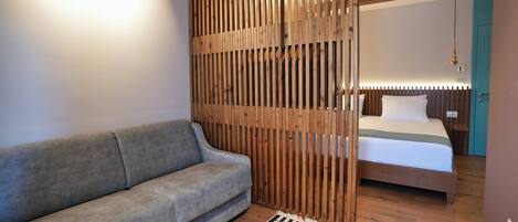 Ein modernes Zimmer mit grauem Sofa, einer Holzwand, einem Bett mit weißer Bettwäsche und einem gemusterten Teppich.