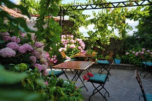 An outdoor patio with stone flooring, wooden tables, and chairs with blue cushions. - Hotel Palorto (Gjirokastër)
