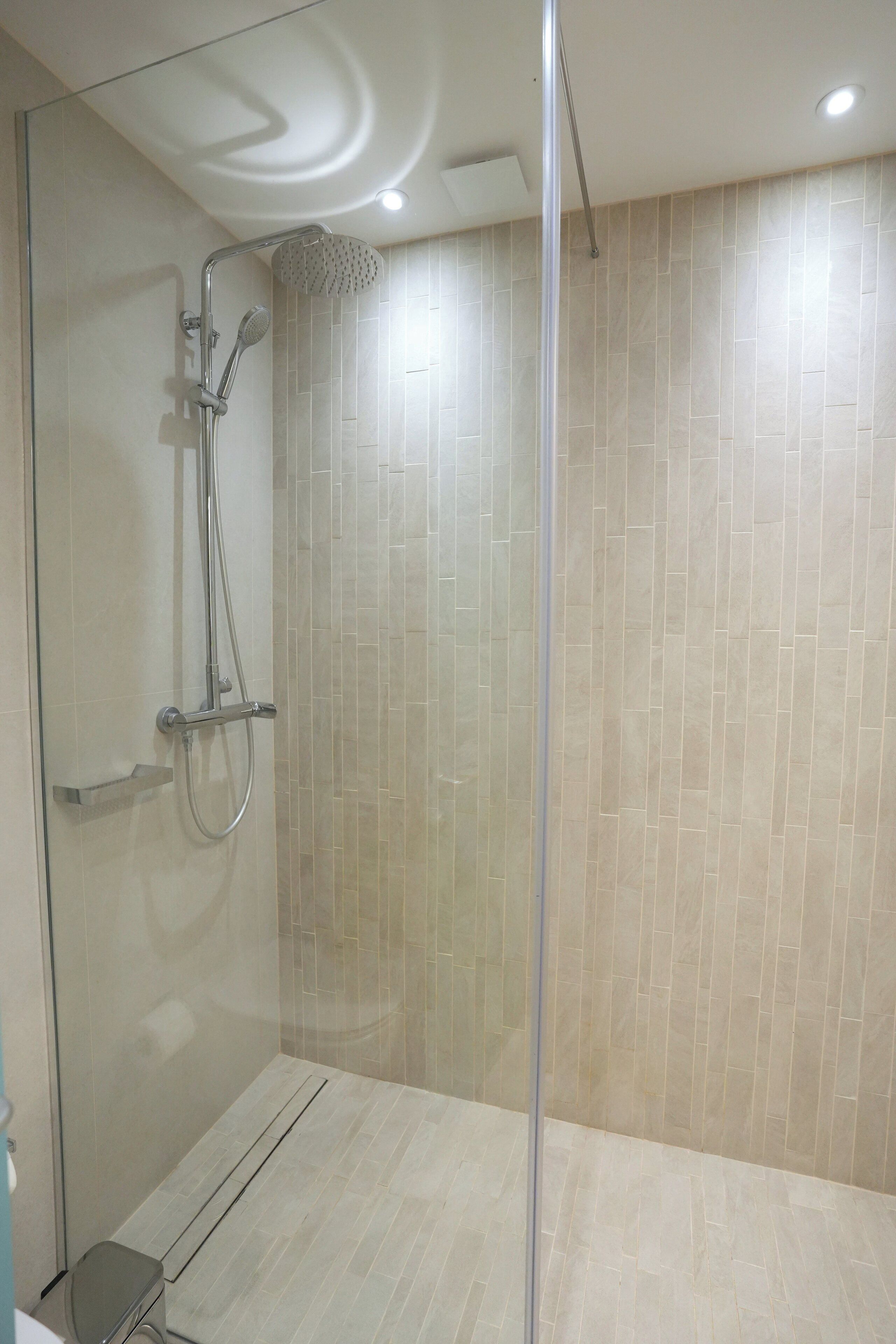 A modern shower with a glass door, a handheld showerhead, and a wall-mounted control panel.