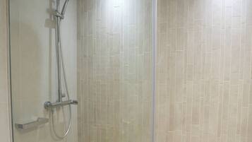 A modern shower with a glass door, a handheld showerhead, and a wall-mounted control panel.