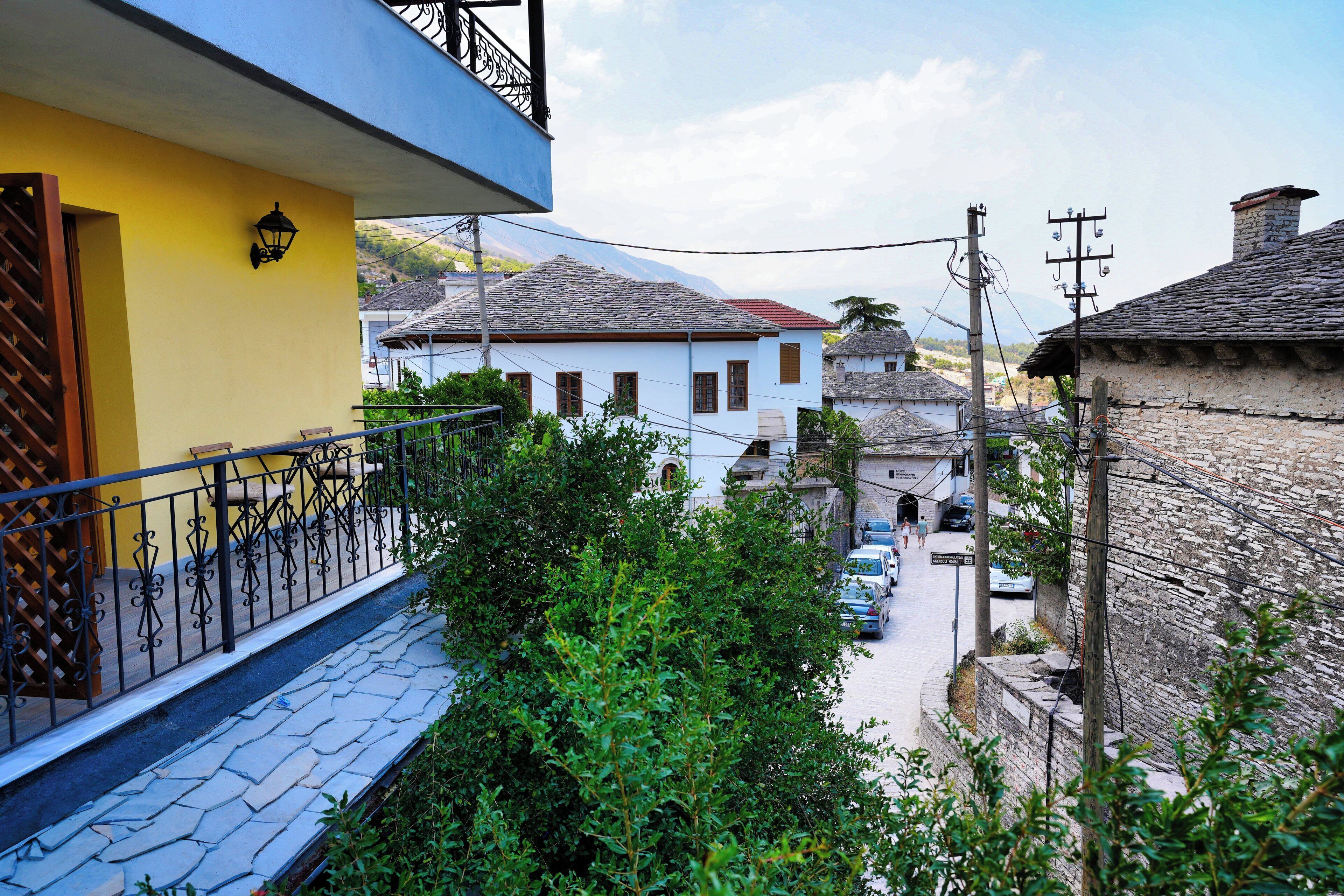 A narrow street with traditional stone buildings, a balcony with a metal railing, and a clear view of the surrounding area.
