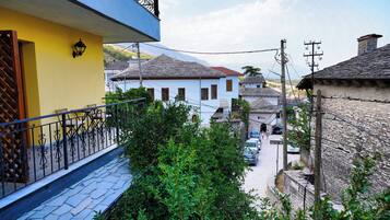 A narrow street with traditional stone buildings, a balcony with a metal railing, and a clear view of the surrounding area.