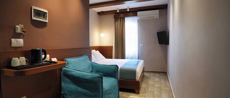 Quarto de hotel com uma cama, uma escrivaninha com cafeteira, um cesto de lixo e um tapete estampado.