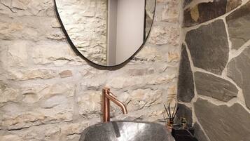 A bathroom with a stone wall, a round mirror, and a copper faucet.