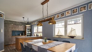 A modern kitchen with a central island, pendant lighting, and a dining area with a table and chairs. - Freester Kapitänshäuser (Kröslin)