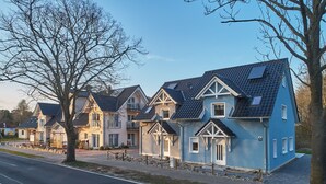 A row of modern houses with gabled roofs and dormer windows, arranged along a street with a sidewalk and a tree-lined road. - Freester Kapitänshäuser (Kröslin)