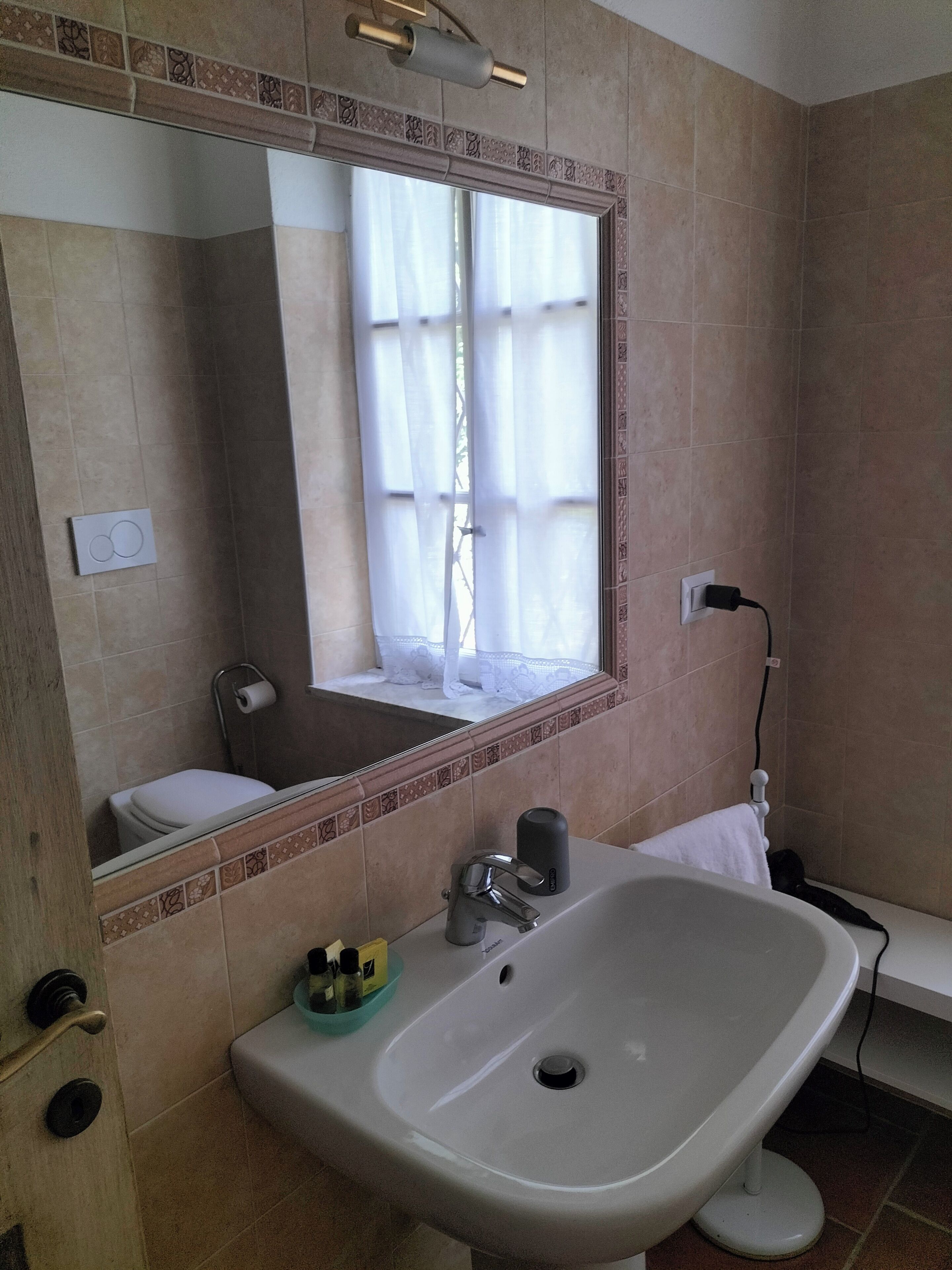 Un bagno con un lavandino ampio, uno specchio, un water e una finestra con tende.