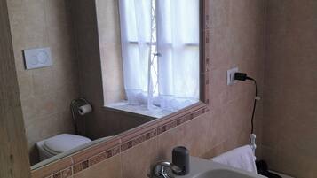 Un bagno con un lavandino ampio, uno specchio, un water e una finestra con tende.