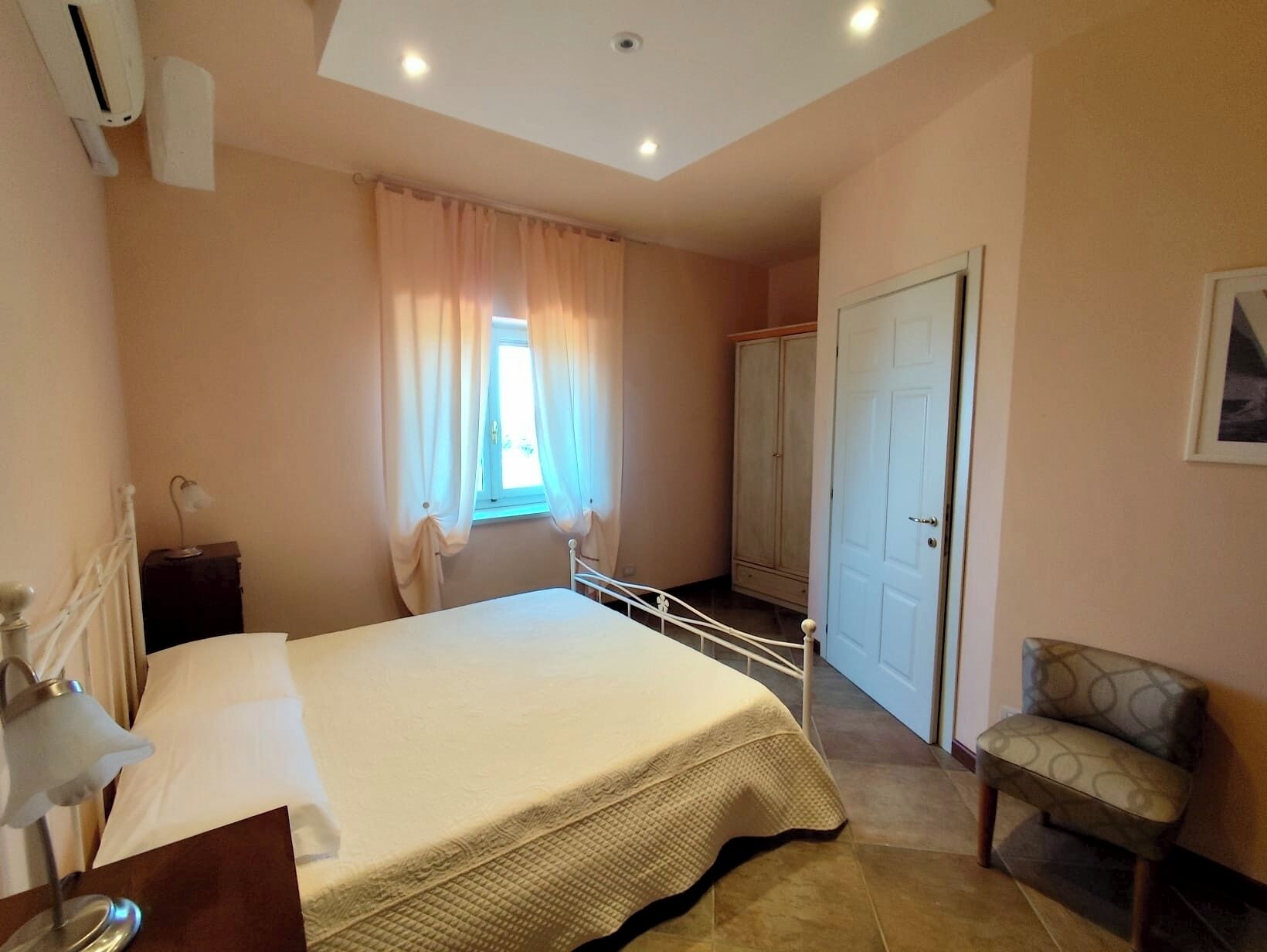A bedroom with a bed, a chair, a wardrobe, and a window with curtains.