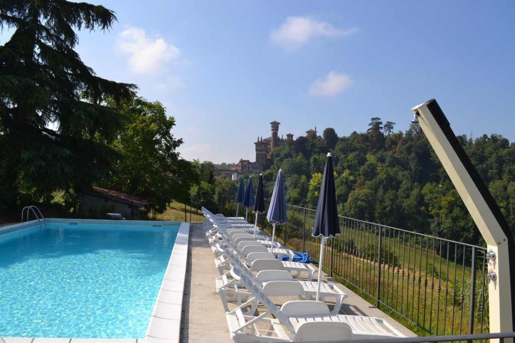 Une piscine entourée d’une clôture et d’arbres, avec des chaises longues et des parasols.