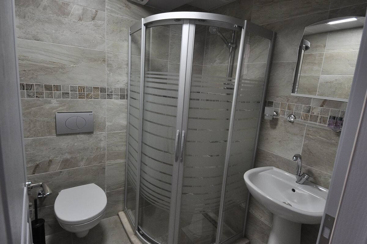 A modern bathroom with a glass-enclosed shower, a toilet, and a sink.