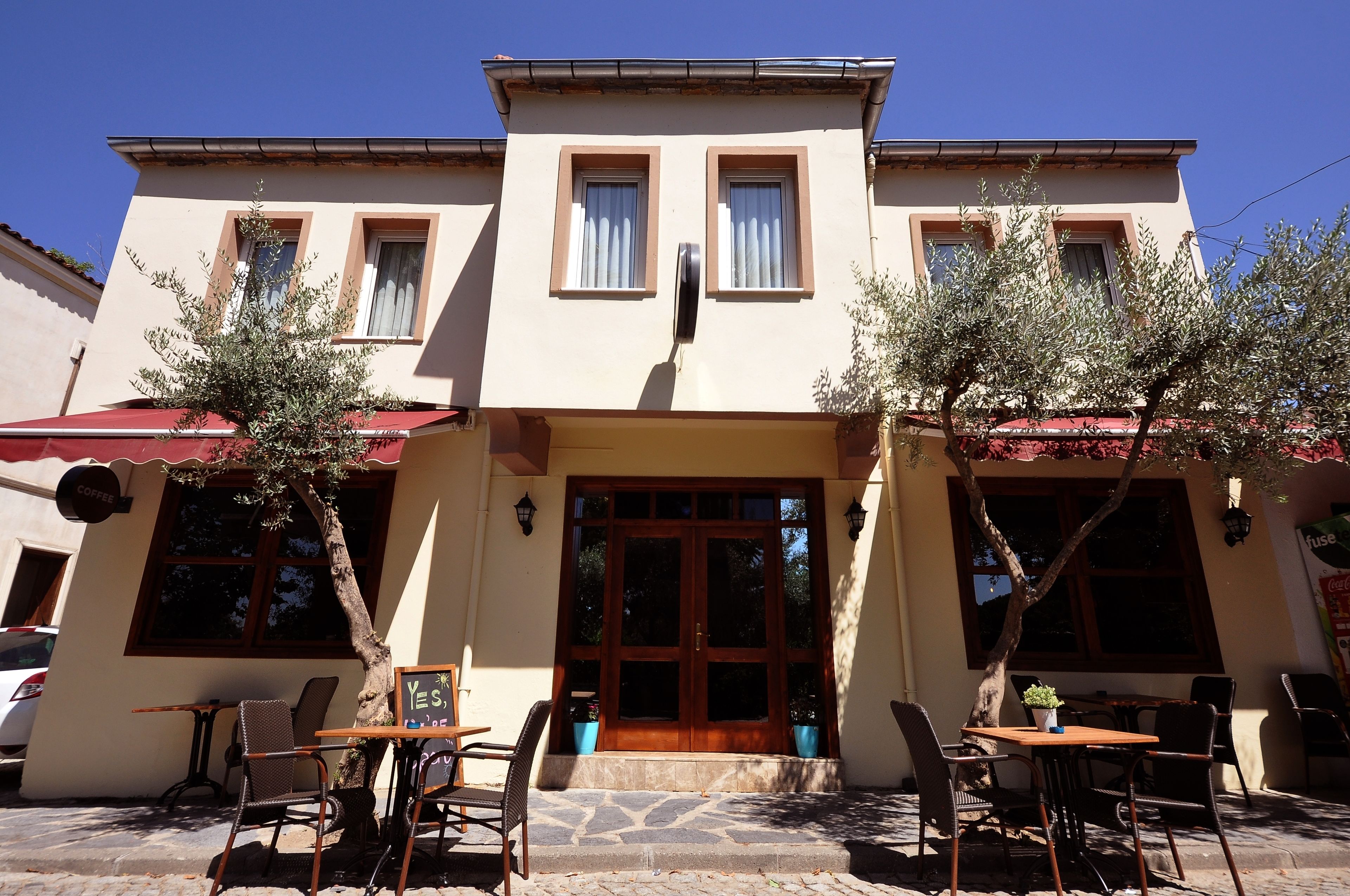 A building with a central entrance, two potted plants on either side, and outdoor seating with chairs and tables.