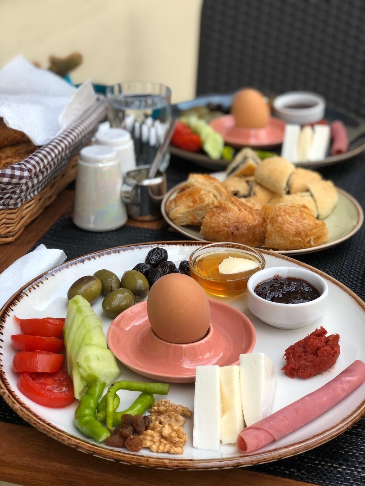 Ein Frühstückstisch mit Tellern voller Speisen, darunter Eier, Oliven, Tomaten, Gurken, Käse und Gebäck.
