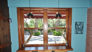 A wooden bar with two hanging pendant lights, a tiled floor, and a view of a garden with trees and a pathway. - Queen Bee Hotel (Selçuk)