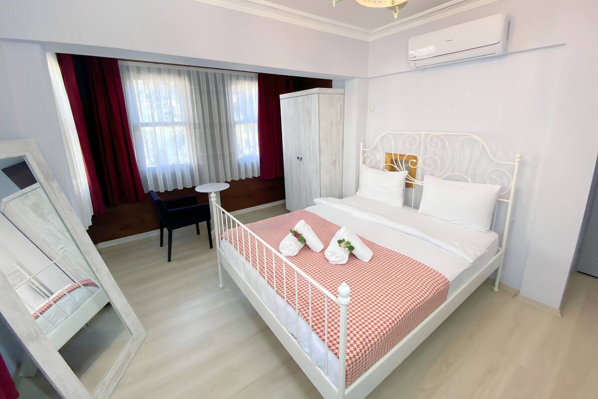 A hotel room with a bed, a desk, a chair, and a mirror.