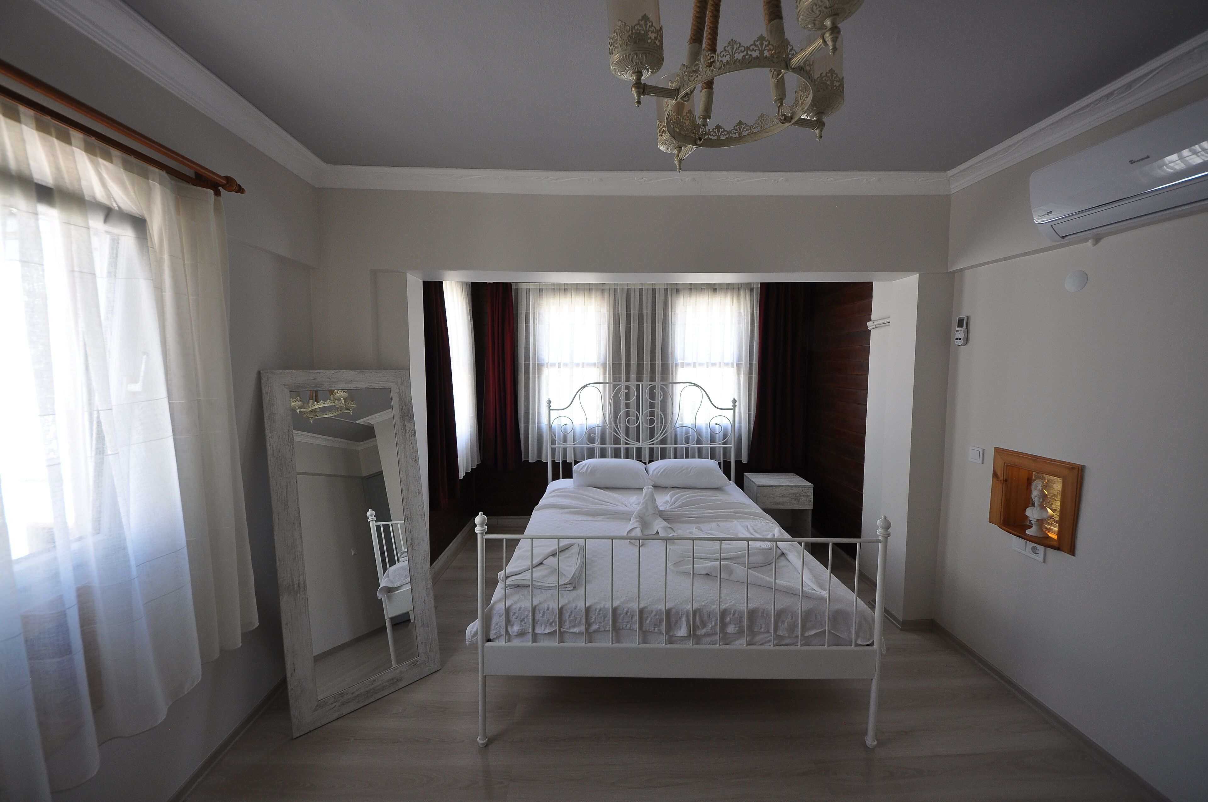 A neatly arranged bedroom with a metal bed frame, a wooden wardrobe, and a chandelier.