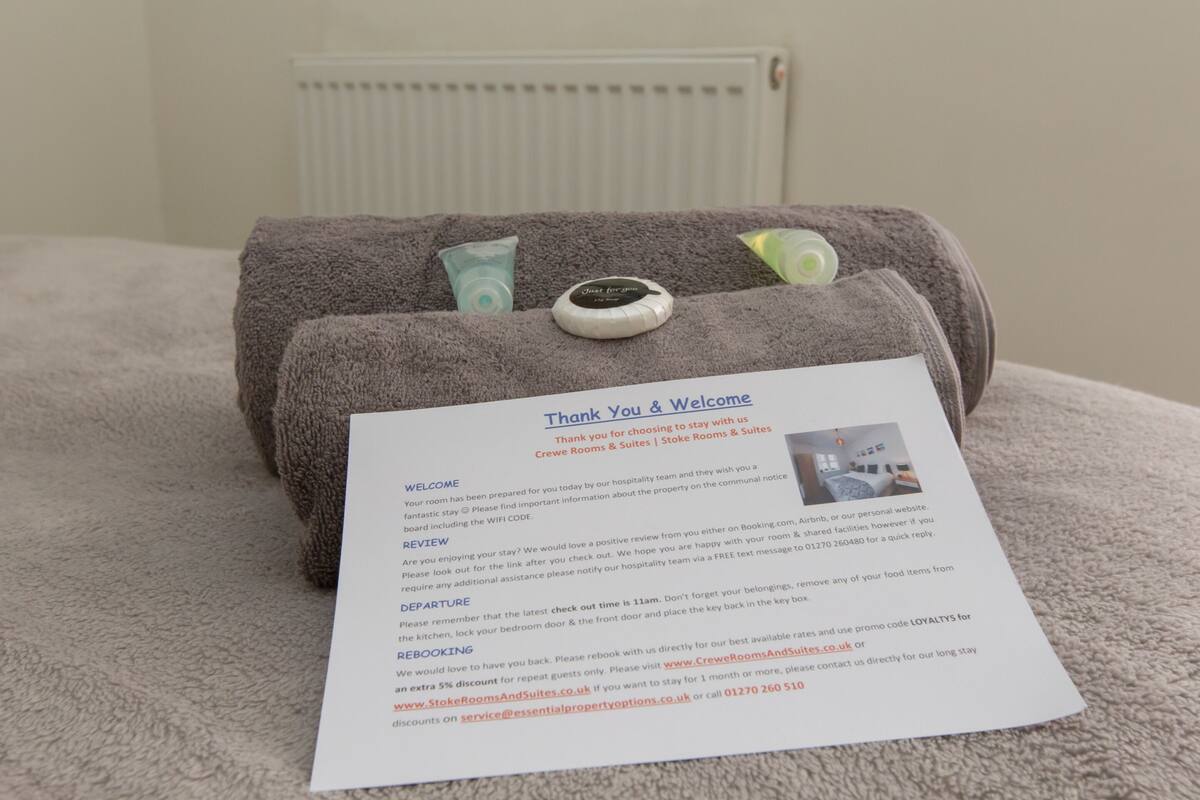Ein Willkommensschild mit einem Handtuch und Toilettenartikeln auf einem Bett.