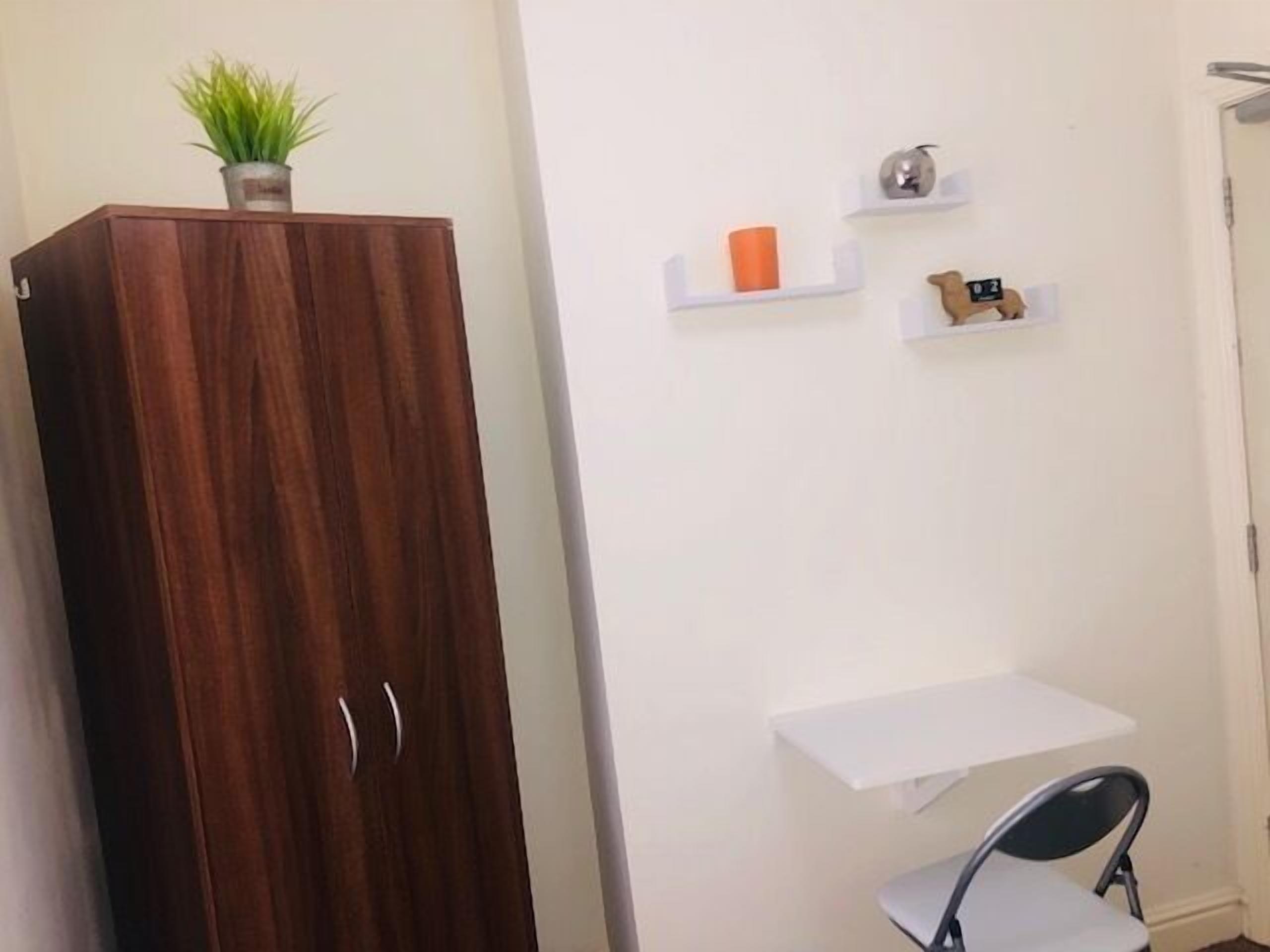 Une pièce comprenant une armoire en bois, un bureau blanc, une chaise et une petite étagère ornée d’objets décoratifs.