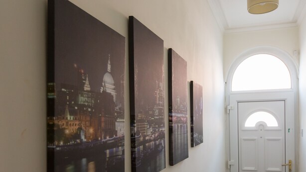 Tres grandes pinturas urbanas en tonos negros sobre una pared, una puerta blanca con un ventanal semicircular y una lámpara en el techo.