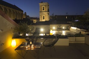 Un patio al aire libre con una mesa lista para comer, rodeada de sillas y una lámpara encendida.