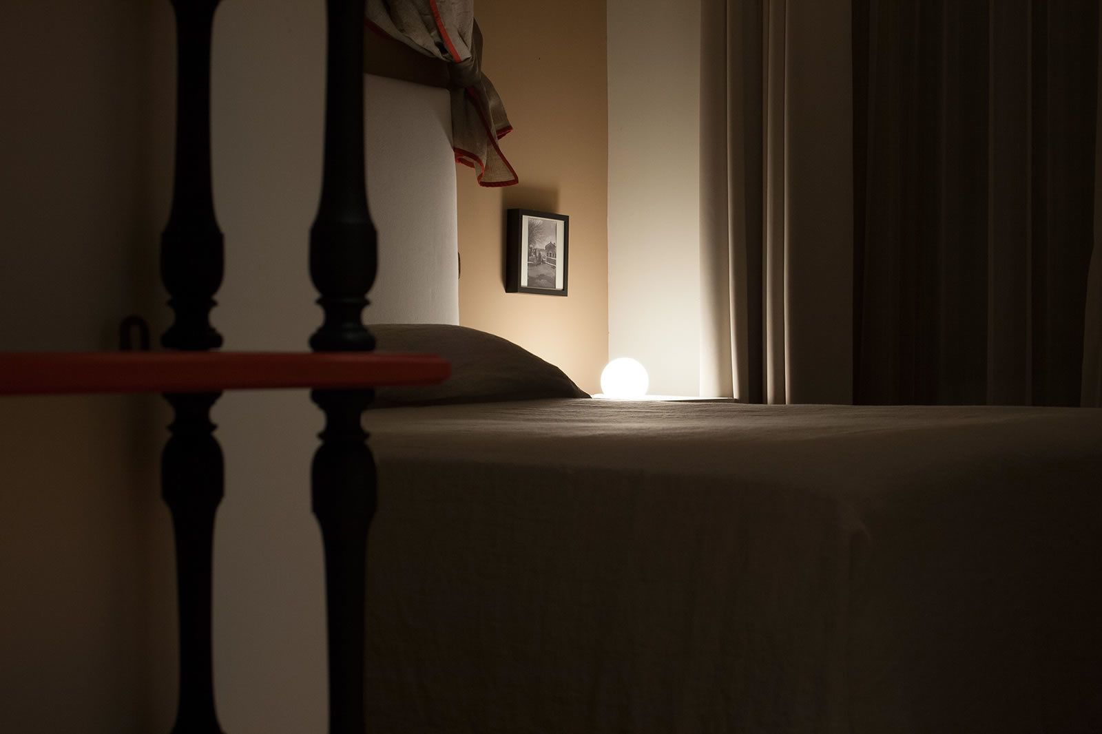 A dimly lit hotel room with a bed, a nightstand, and a framed picture on the wall.