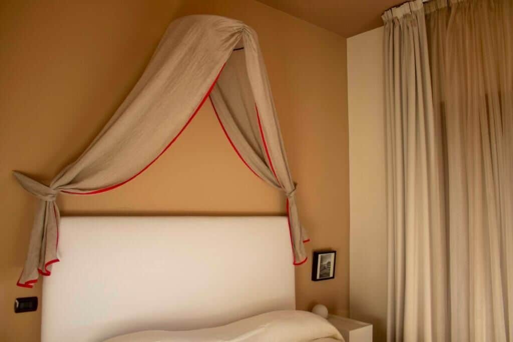 Une chambre à coucher comprenant un lit, une table de chevet, une commode, une horloge murale et une fenêtre avec des rideaux.