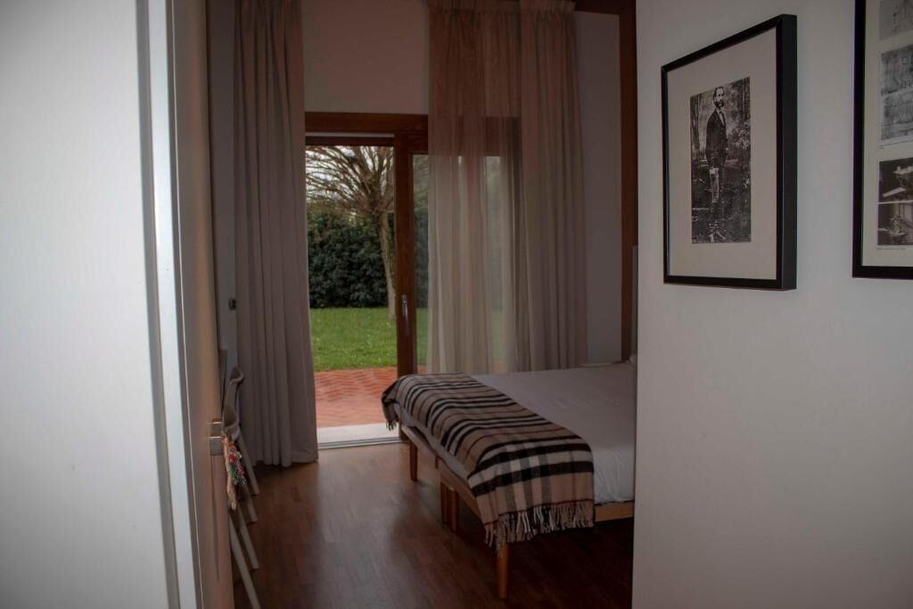 Une chambre à coucher avec un lit, une porte donnant sur un jardin et un tableau encadré accroché au mur.