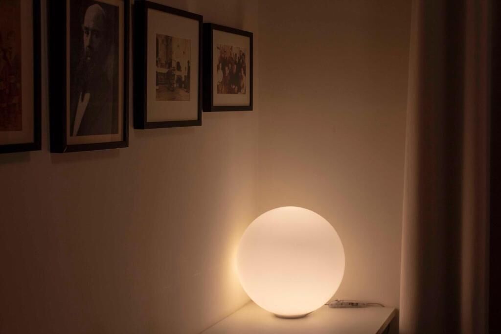 A wall with framed pictures and a round, illuminated table lamp.