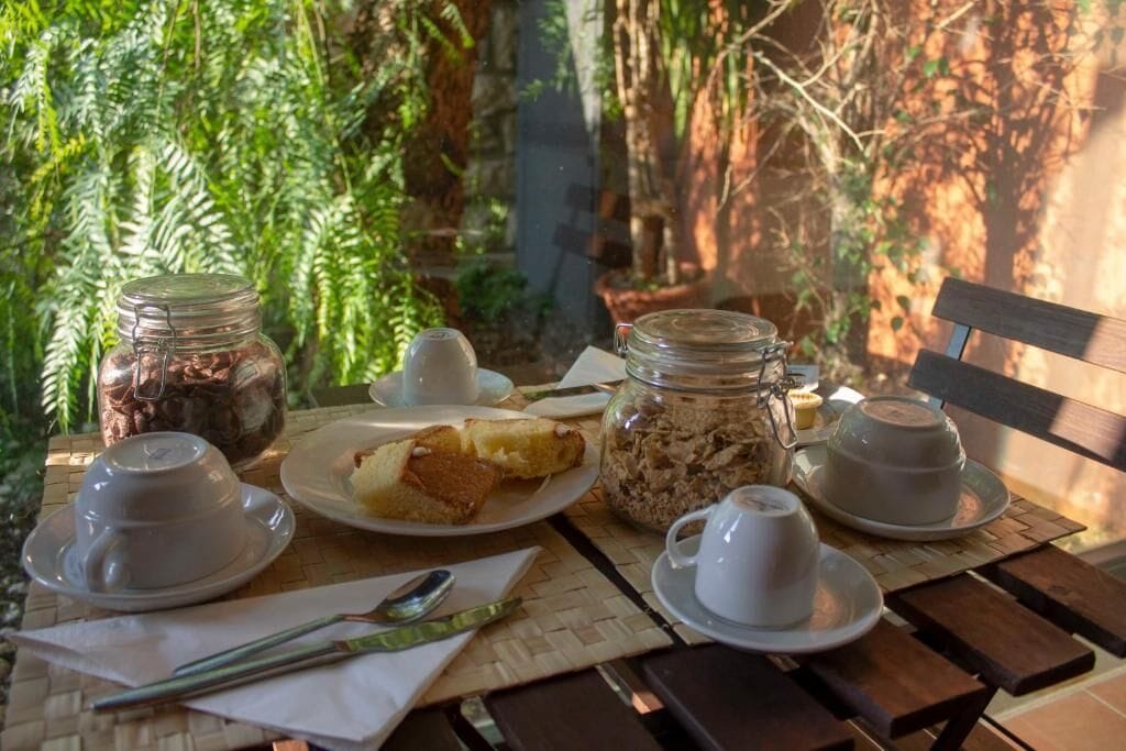 A table set with a plate of food, two cups, a jar of coffee, and a bench.