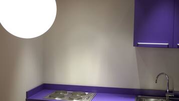 A modern kitchen with a purple countertop, stainless steel sink, and a round light fixture.