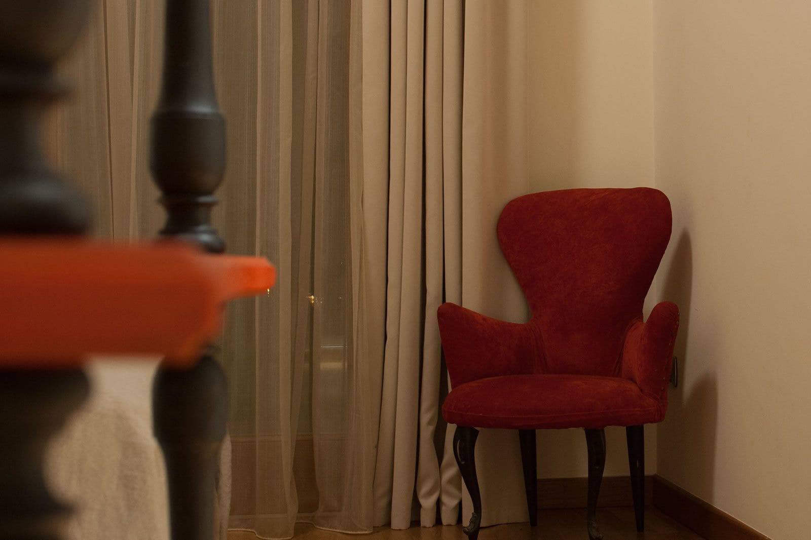 Una habitación con un sillón rojo, una silla de madera y una puerta con cortinas translúcidas.