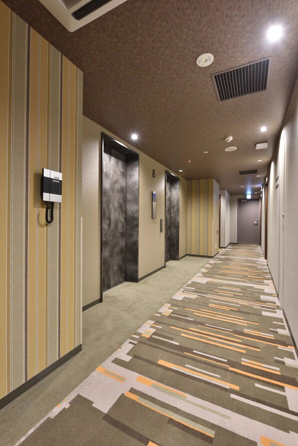 Un pasillo de hotel con paredes a rayas, una alfombra estampada y varias puertas que dan a las habitaciones.