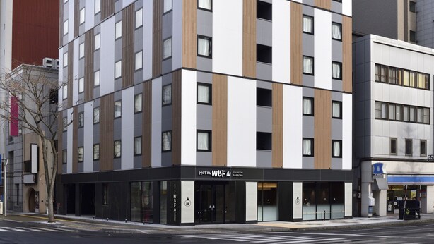 Un hotel moderno con diseño de varios pisos, que presenta una combinación de paneles blancos y marrones, ventanas amplias y un letrero visible del hotel.