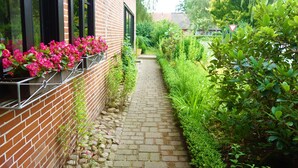 A brick building with a narrow stone pathway leading to a gate. - Ferienwohnung Schuster (Garlstorf am Walde)