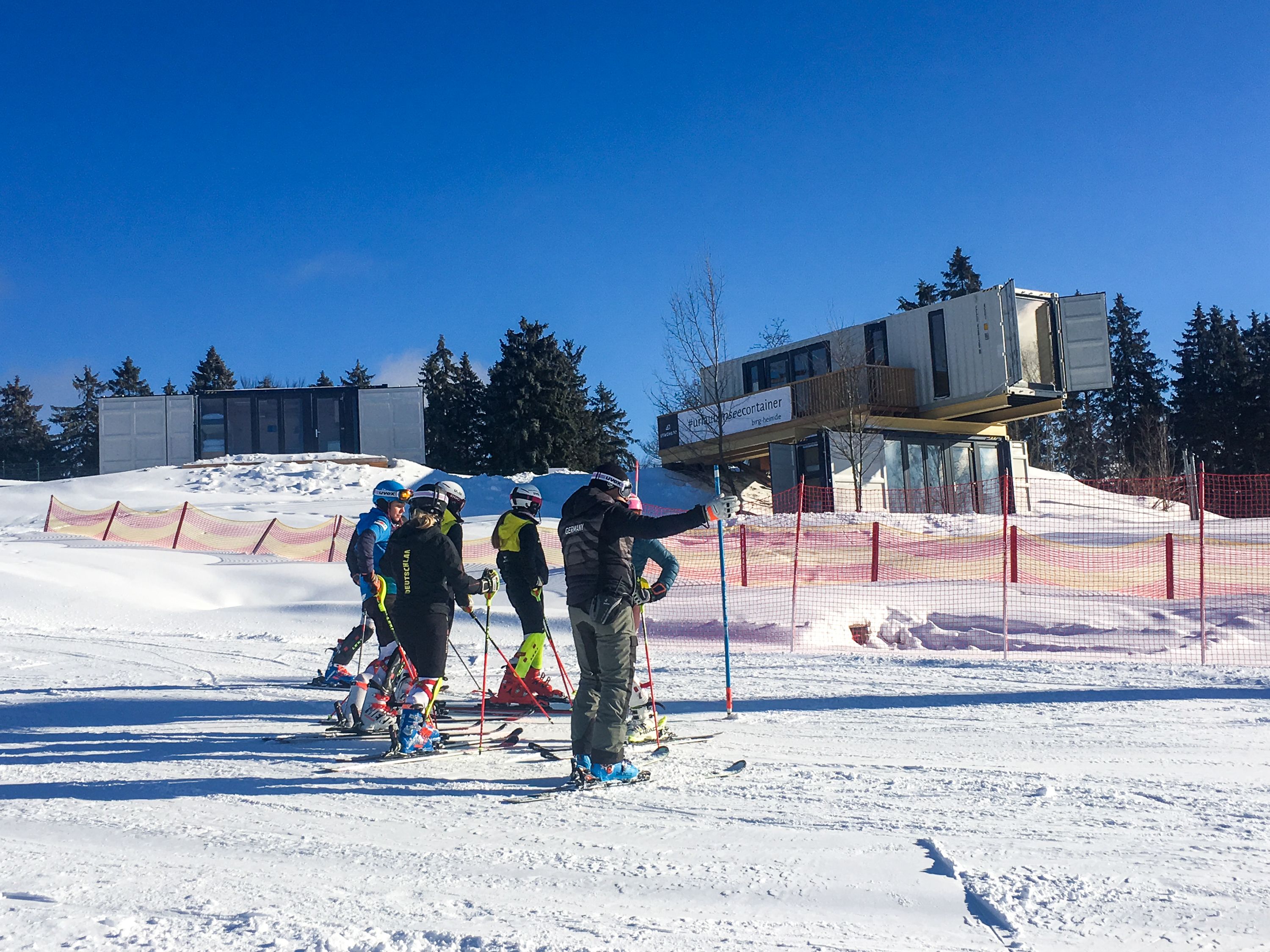A group of people on skis in a snowy area with a building in the background.